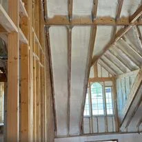 Interior wooden framing with exposed studs and ceiling joists prepared for insulation installation