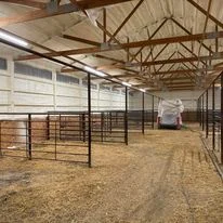 Interior of agricultural building with insulation installation, exposed wooden beams, metal framing, and dirt flooring