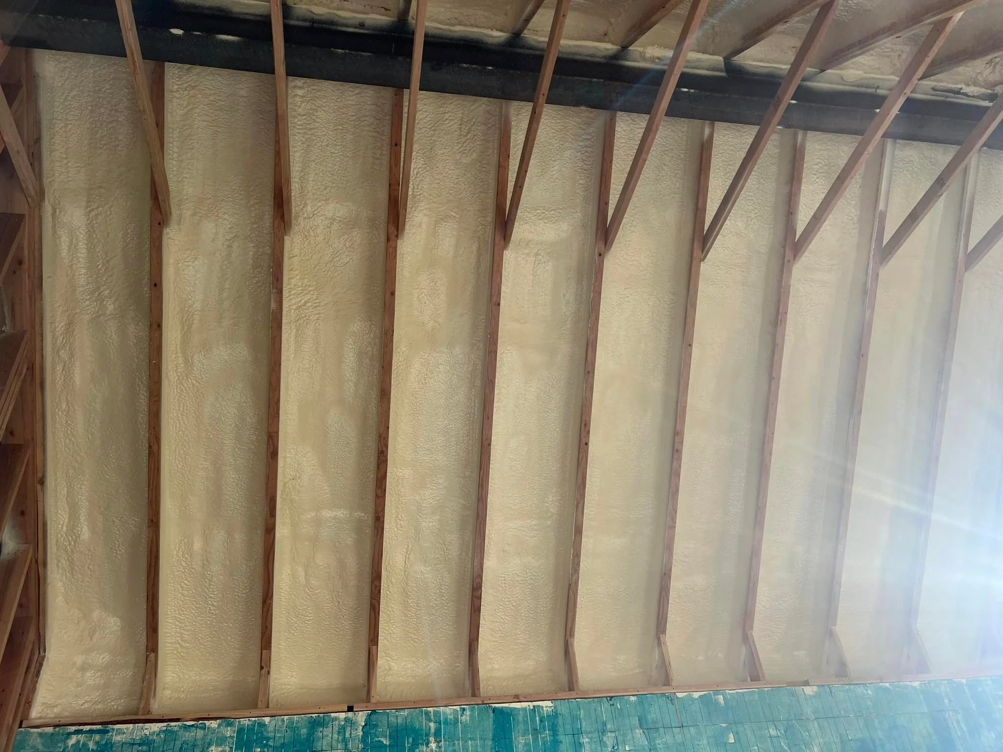 Spray foam insulation applied between wooden roof rafters in residential attic space