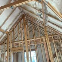 Interior residential framing with exposed studs and roof trusses ready for insulation installation