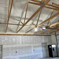 Spray foam insulation applied to warehouse ceiling cavity between wooden rafters