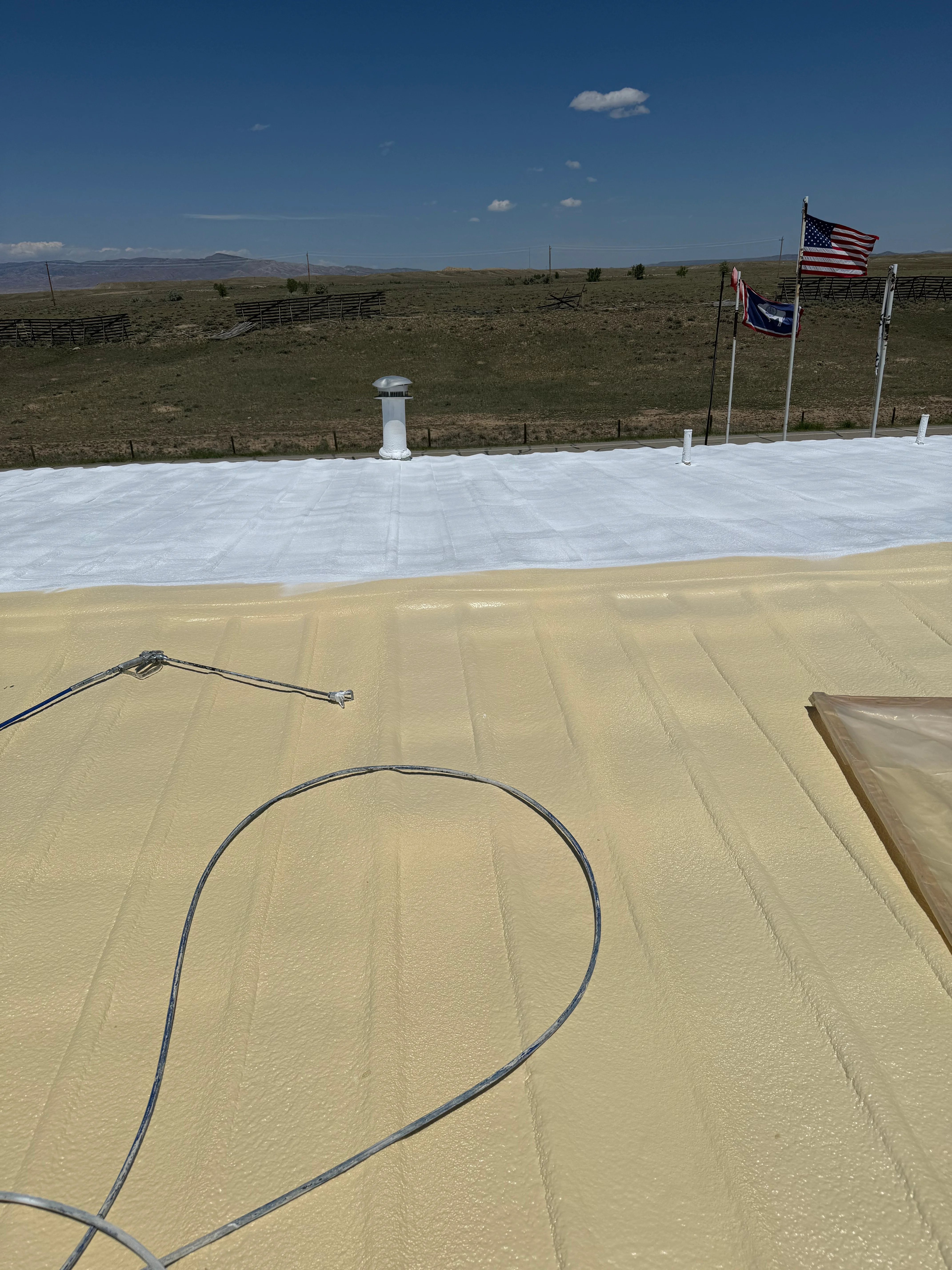 Spray foam insulation installation on roof with drainage lines and white vapor barrier