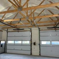 Garage interior with foam insulation installed in ceiling and wall cavities between wooden rafters