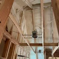 Interior view of open wood framing with foam insulation installed between studs and ceiling joists