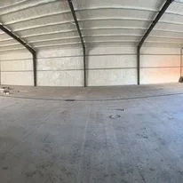 Interior of metal warehouse building with insulation installed on ceiling and walls above concrete floor
