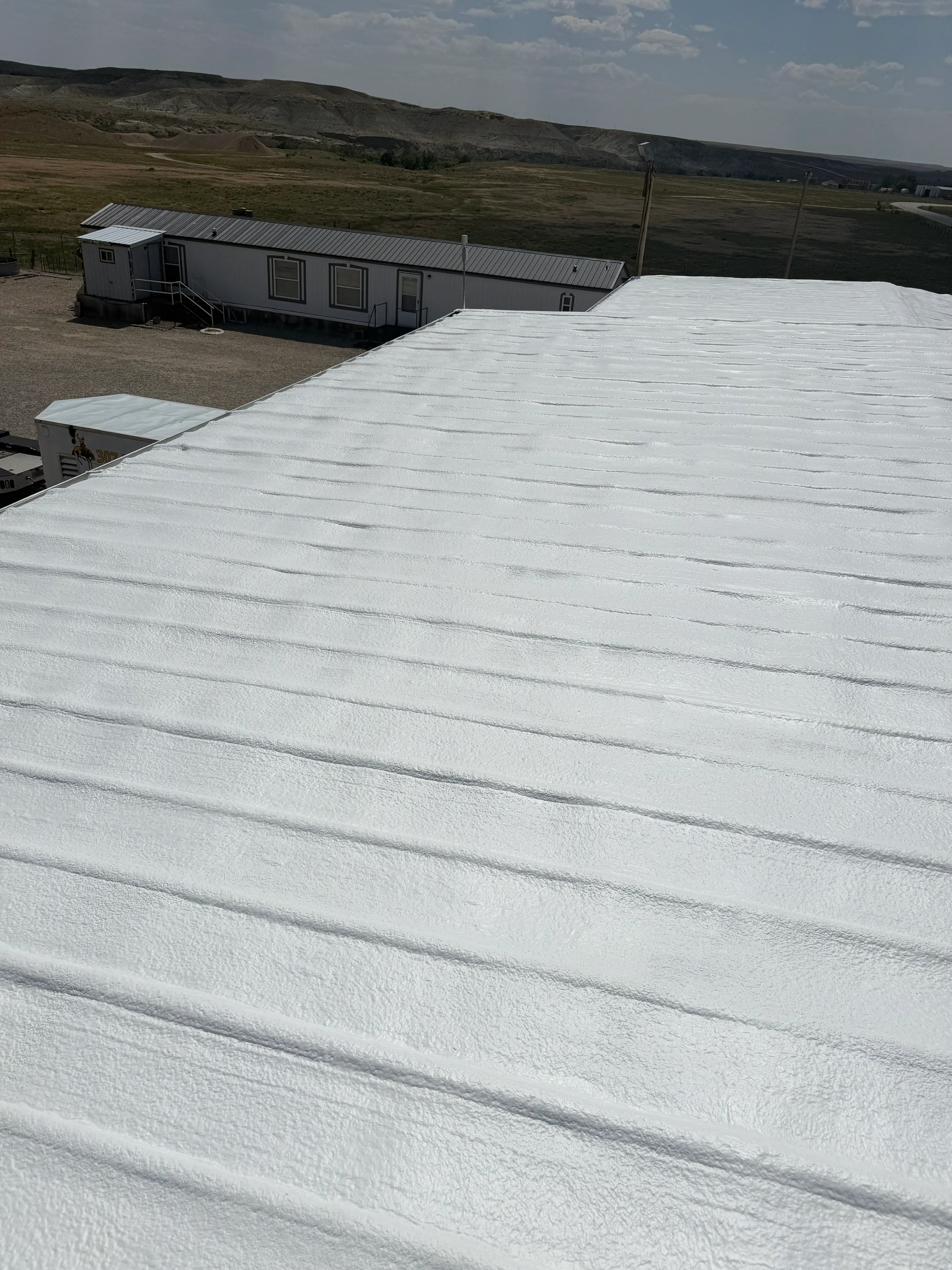 White spray foam insulation covering large commercial roof with modular buildings in background