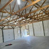Interior of commercial warehouse with exposed wooden beam roof structure and newly installed foam insulation on ceiling and walls