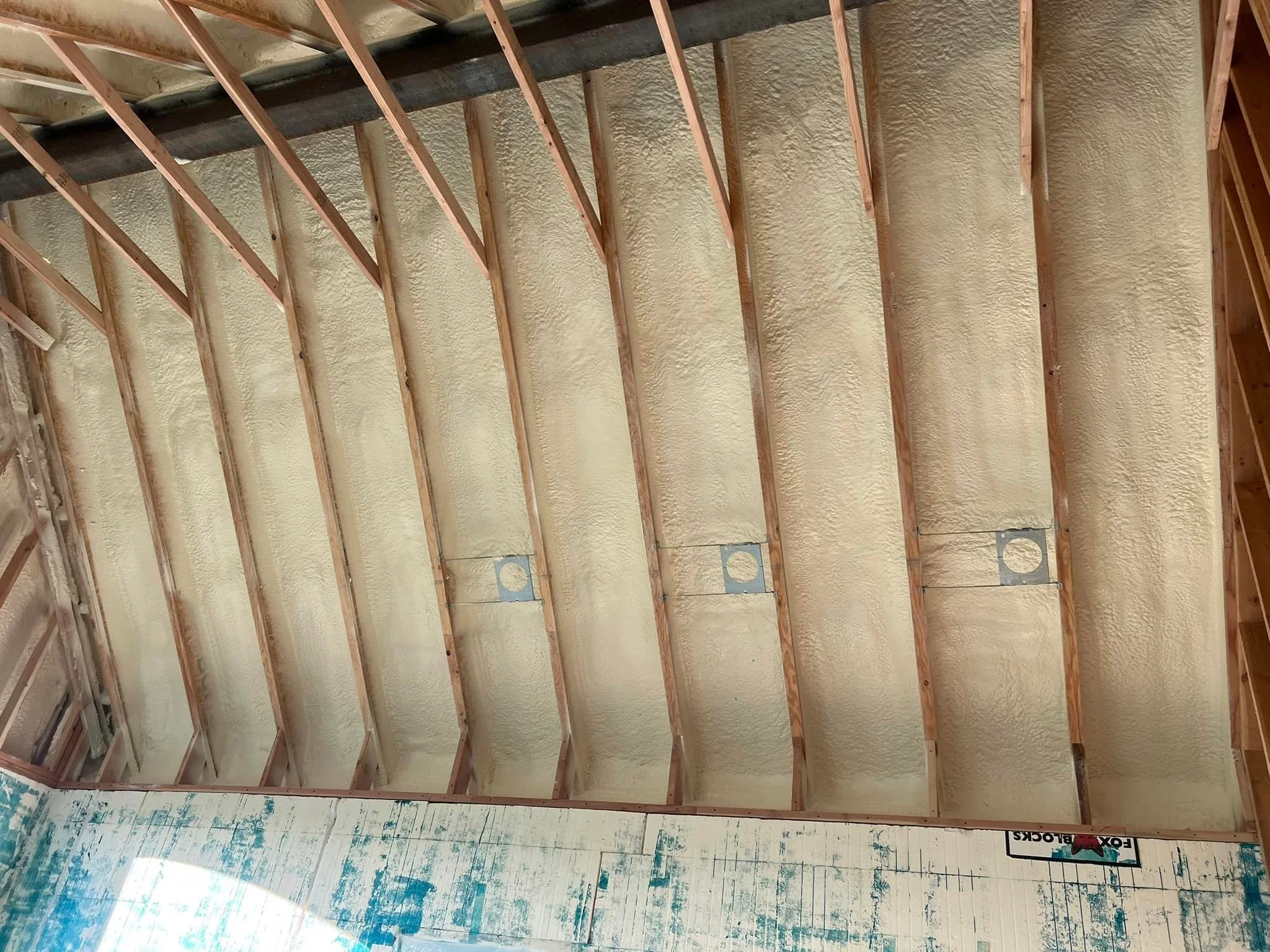 Spray foam insulation installed between roof rafters with outlet boxes cut into foam