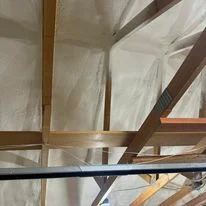 Spray foam insulation applied between wooden ceiling joists and beams