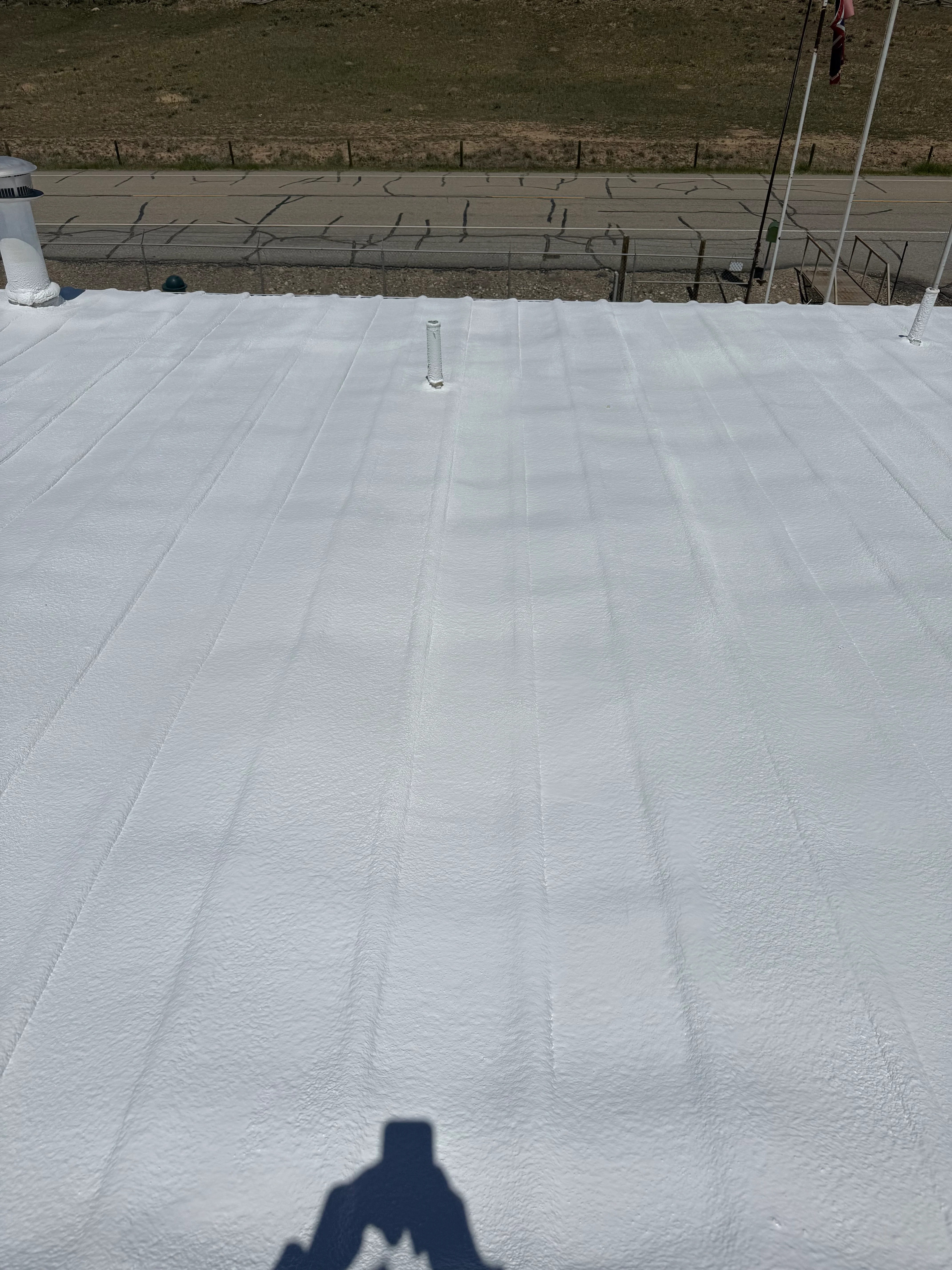 White spray foam insulation covering flat roof with seams and pipe penetrations visible