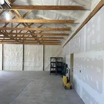 Interior warehouse with exposed wooden beams, white drywall installation, and insulation materials in progress