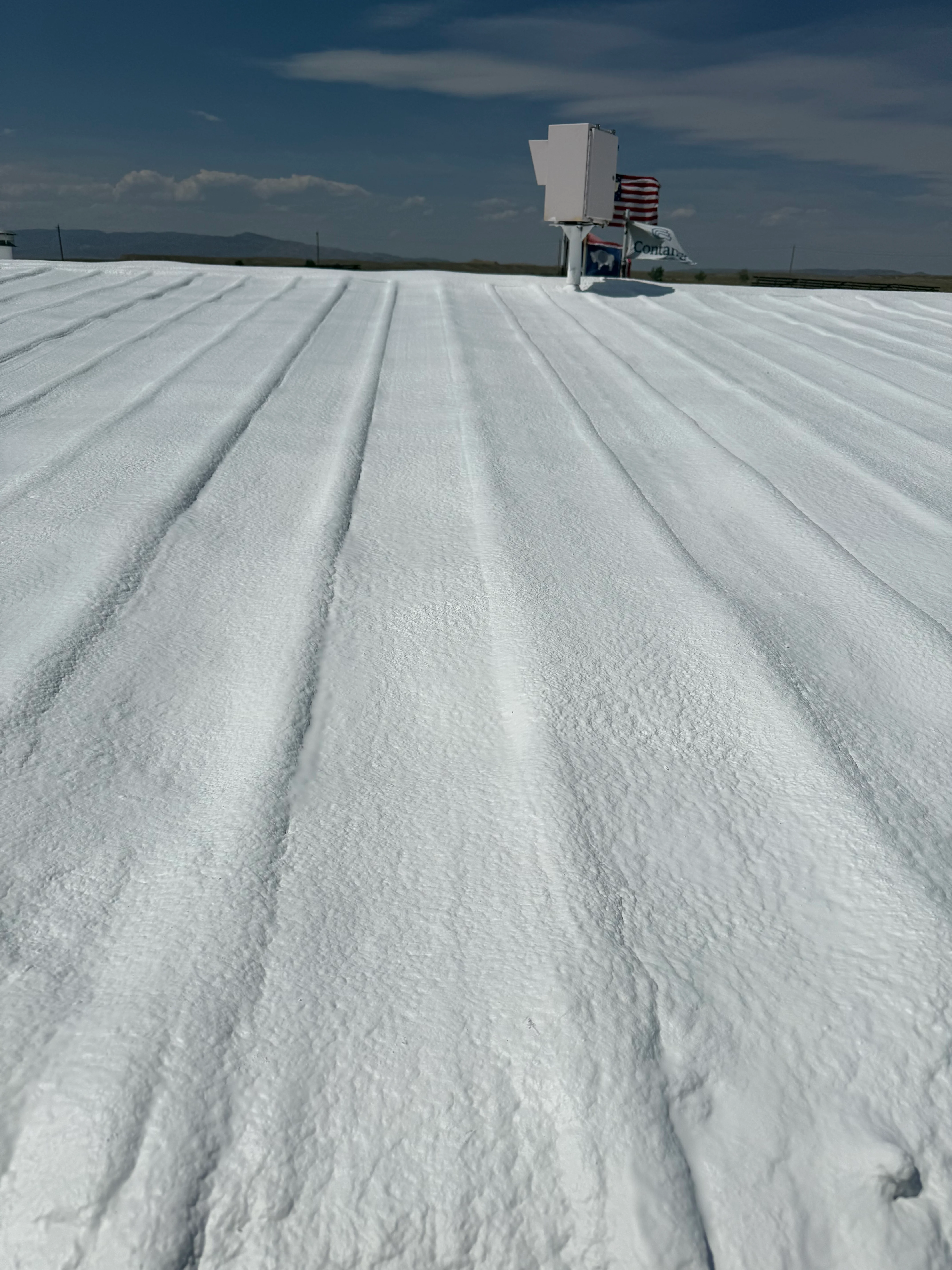 Spray foam insulation installed on commercial flat roof with uniform ridge patterns and application equipment