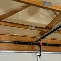 Spray foam insulation applied to ceiling with wooden beams and mechanical systems visible