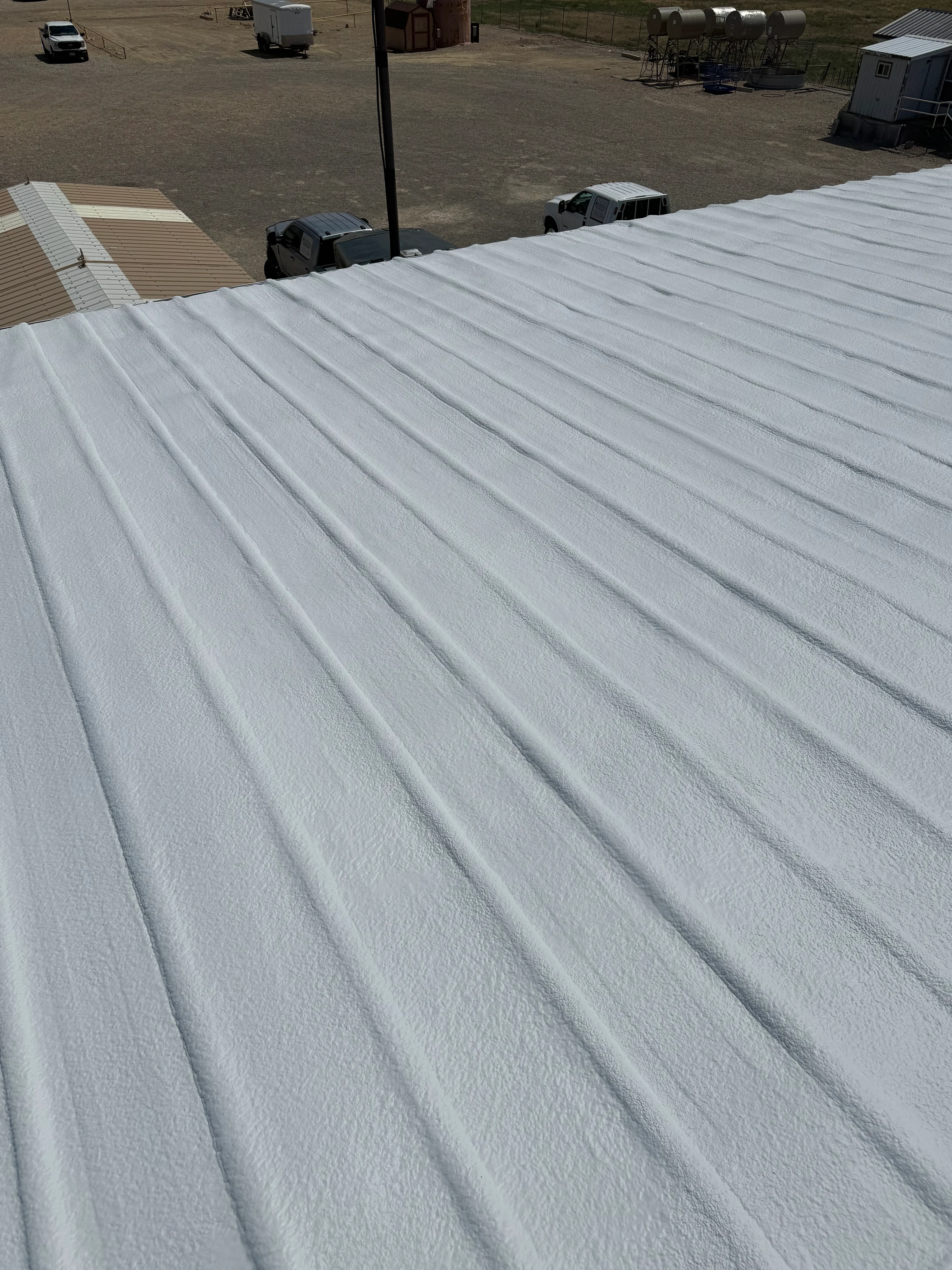 White spray foam insulation applied to commercial metal roof with rural facility in background