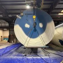 Industrial spray foam insulation being applied to large cylindrical tank with blue protective covering