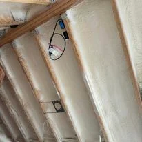 Spray foam insulation applied to ceiling joists and framing with electrical wiring visible